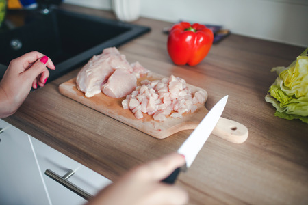 Female hands cutting raw chicken on wooden desk in modern kitchen.の写真素材