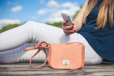 Young girl sitting on a wooden bridge by the water using a white mobile phone.の写真素材