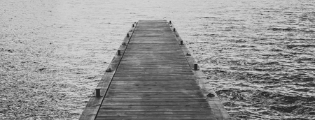 Black and white panoramic photo of a wooden bridge on the water.