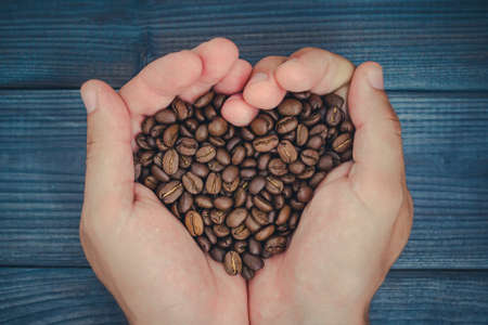 Male hands holding coffee seeds in heart shape symbol of love.の写真素材