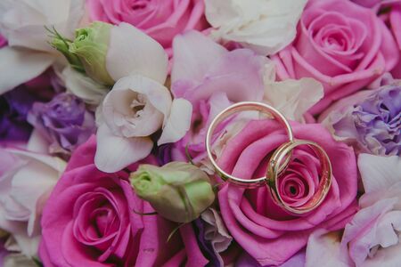 Golden wedding rings on flowers bouqet made of white and pink roses.の写真素材