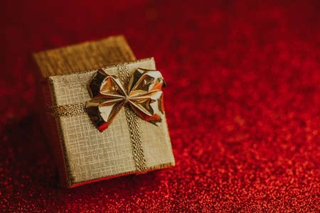 Golden shiny gift box with ribbon on red glitter background.の写真素材