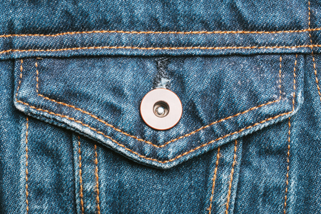 Blue jeans fabric pocket with metal button. Grunge used fashion jacket background.