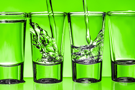 Pouring vodka into transparent vodka shot glass. Green weekend party alcohol background.の写真素材