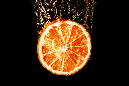 Orange slice splashing into water on black background.の写真素材