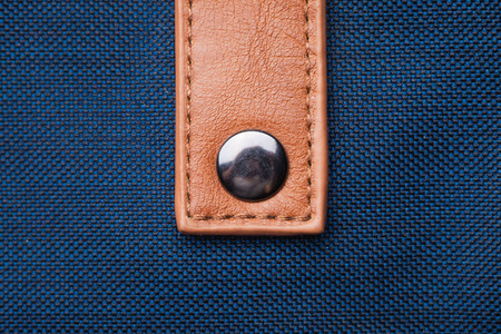 Brown leather strap attached to blue fabric. Fashionable hand bag closeup texture.