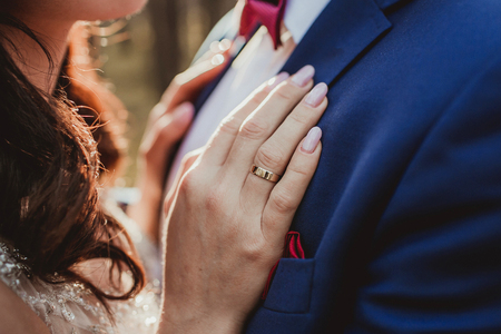 Golden wedding ring on bride`s finger. Romantic sunset hug with hand on groom`s suit. Wedding fashion and details background.の写真素材