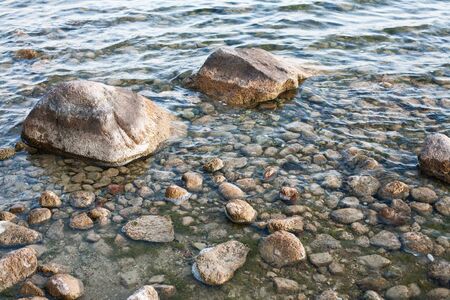 Rough stones on lake shore. Wet rocky beach water background.の写真素材