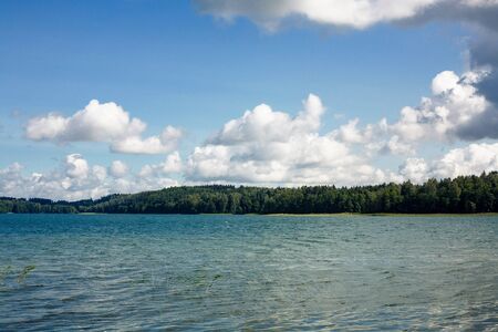 Summer lake in forest landscape. Blue cloudy sky over water surface panoramic view.の写真素材