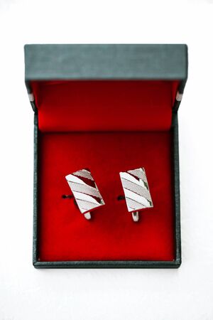 Silver cufflinks in red box isolated on white. Mens groom fashion accessory background.