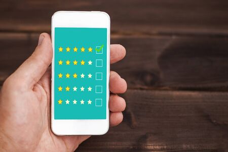 Internet satisfaction survey. Quality review at home. Rate us site. Customer rating background. Holding mobile phone in hand.の写真素材