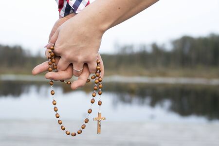 Couple pray together. Hands holding rosary symbol of love to God. Catholic religion cross. Walking together through the life outdoor background.の写真素材