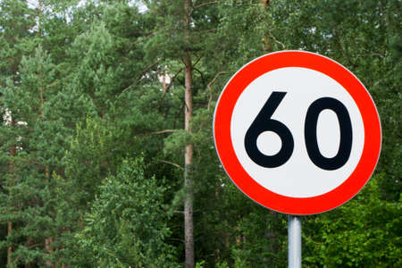 Speed limit sign with trees behind. Maximum sixty kilometers per hour. Safety on road in forest background. White round sign red border line.の写真素材