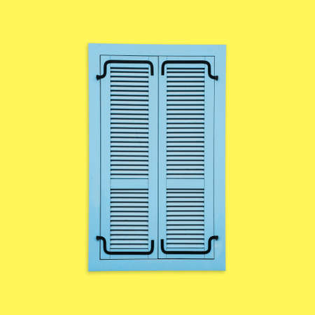 Blue wooden window shutter. Yellow paint wall. Closed window isolated. European style architecture background.の写真素材