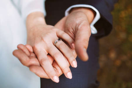 Married couple. Bride and groom holding each other hands. Wedding jewelery. Engagement ring on a finger.の写真素材