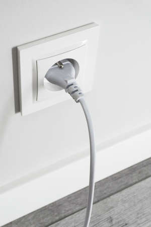 Brand new electrical socket isolated on gray wall. White wire plug plugged in. Renovated studio apartment power supply background. Empty copy space white plastic power outlet.の写真素材