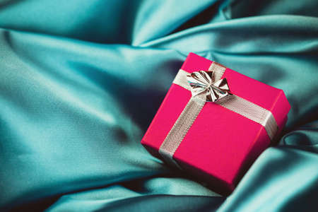 Small pink gift box. Silver shiny ribbon. Christmas present background. Empty copy space surprise...
