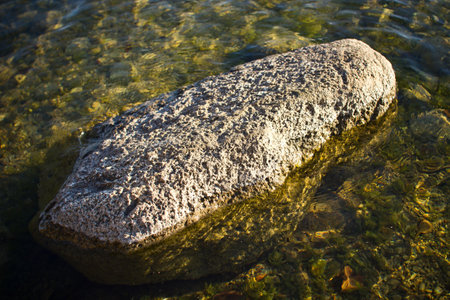 Big stone in water. Lake shore rock background. Single stone on the bottom of the lake.の写真素材