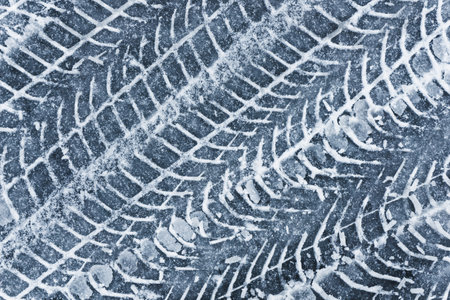 Snow tire mark. Asphalt covered in snow. Dangerous road conditions. Car imprint on frozen ground. Tire trail on ice.の写真素材