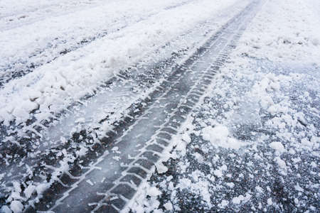 Snow tire mark. Asphalt covered in snow. Dangerous road conditions. Car imprint on frozen ground. Tire trail on ice. City streets covered in snow during heavy snow fall. Slippery road background.の写真素材