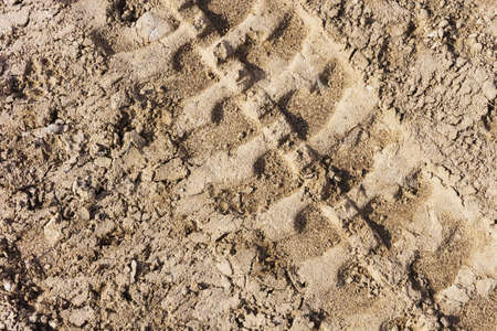 Tire mark background. Tire track shape. Trail lines on dry brown sand pattern. Road construction site backdrop. Heavy machinery imprint. Dried mud vehicle wheel shape.の写真素材
