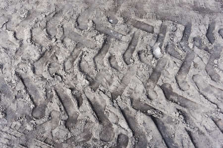 Black sand tire mark background. Tire track shape. Gray gound car imprint. Trail lines on dry sand pattern. Road construction site backdrop. Dried mud vehicle wheel shape.の写真素材