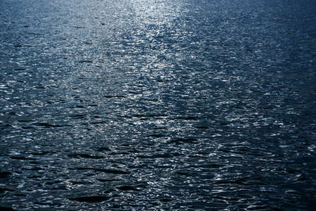 Blue water surface texture background. Natural pattern of water surface with sun reflection.の写真素材
