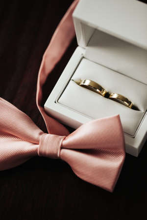 Wedding fashion background. Golden wedding rings. White gift box. Pink bow tie. Wooden table wedding...