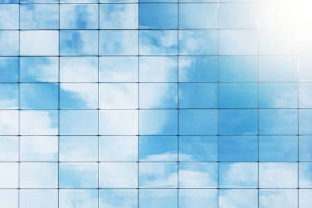 Reflection of blue sky and white clouds in glass window of modern office buildingの写真素材