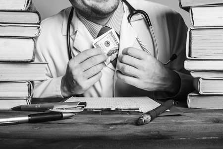 Doctor sitting at desk with stethoscope and money, black and whiteの写真素材