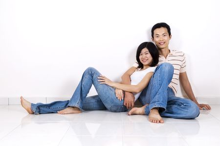 Young Asian adult couple sitting together on tiles floor in home smiling.の写真素材