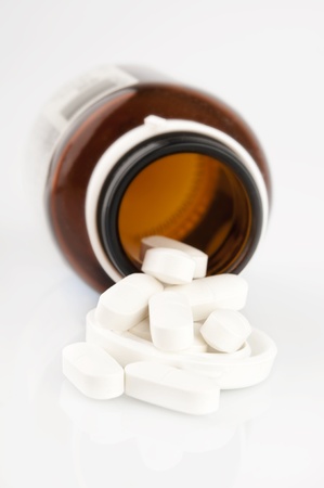 Pills spilled out of a bottle and scattered on white background.の写真素材