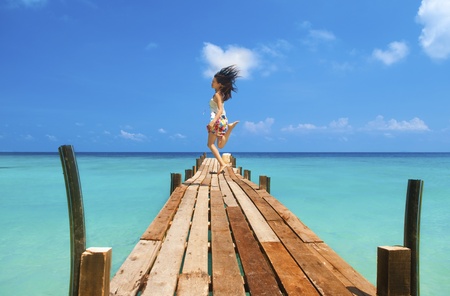 Pretty young girl is jumping up in the air at the beach jettyの写真素材