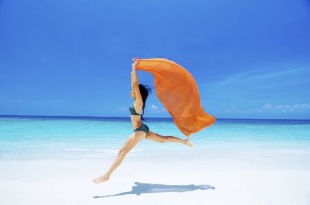 Pretty young bikini girl is jumping up in the air at the beachの写真素材