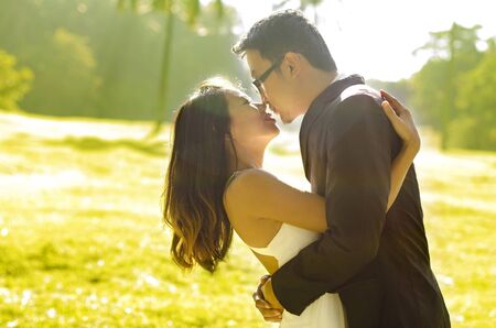 Bride and groom kissing in the park, back-lit in the morning.の写真素材