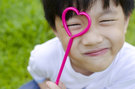 Cute Asian boy holding a heart shape on his eyeの写真素材