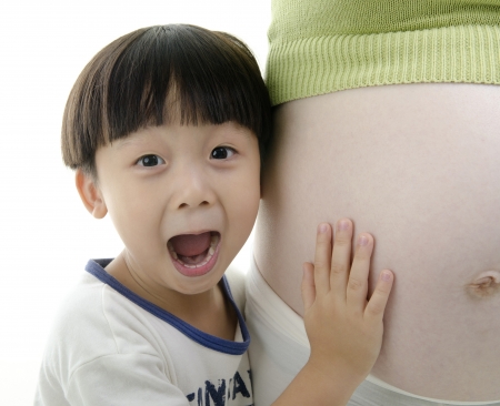 A shot of a little surprising Asian boy listening to her pregnant mother bellyの写真素材