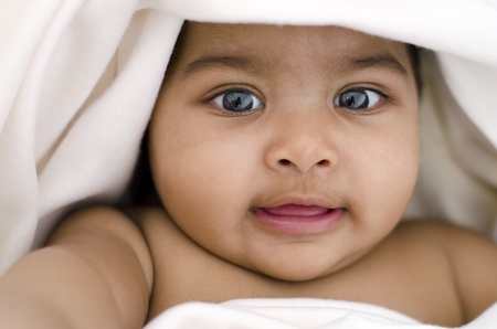 6 months old Indian baby girl smiling, lying on bed and covered by blanketの写真素材