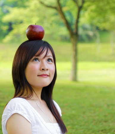 Beautiful young Asian woman with red apple on her head.の写真素材