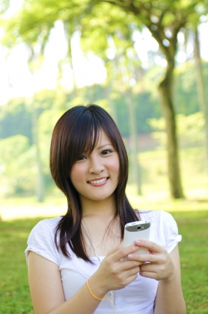 Happy oriental Asian young student using mobile phone to online / texting / sms , outdoor green parkの写真素材