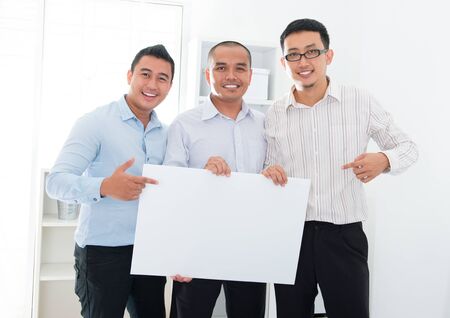 Southeast Asian business team holding a blank banner in officeの写真素材