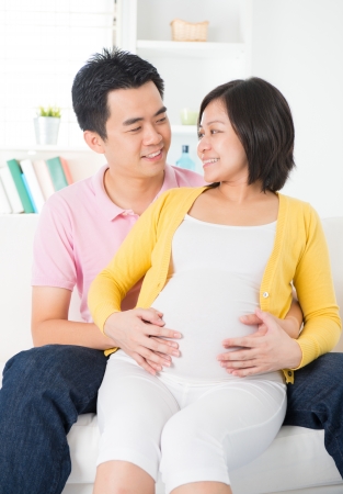 Asian Chinese couple. Husband and 8 months pregnant wife sitting on sofaの写真素材