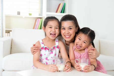 Happy Asian mother and daughters drinking milk at homeの写真素材