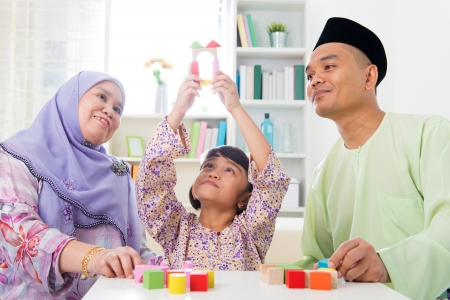 Malay family at home. Muslim girl building a wooden toy house. Southeast Asian parents and child living lifestyle.の写真素材