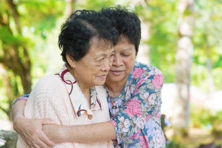 Candid shot of an Asian mature woman hugs and consoling her crying old mother at outdoor natural park. の写真素材
