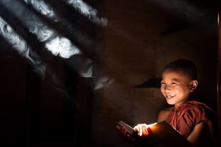 Southeast Asian little monk reading book inside monastery, beautiful natural light shining thru.の写真素材