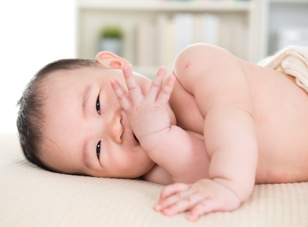 Adorable six months old Asian baby girl lying on bed biting fingers.の写真素材
