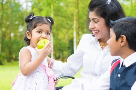 Happy Indian family. Asian girl eating an green apple at outdoor with mother and sibling.の写真素材
