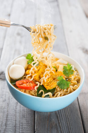 Spicy curry instant noodles holding with fork. Asian cuisine, ready to serve on wooden dining table setting. Fresh hot with steamed smoke.の写真素材