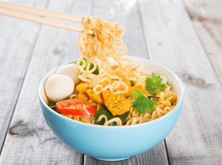 Spicy curry instant noodles with chopsticks. Asian cuisine, ready to serve on wooden dining table setting. Fresh hot with steamed smoke.の写真素材